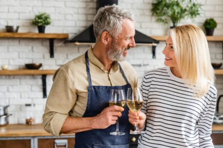 Happy senior couple drinking wine at kitchen while cooking