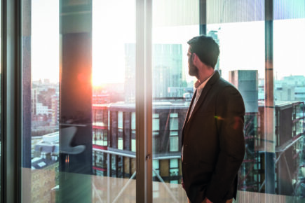 Businessman looking through office window in sunlight