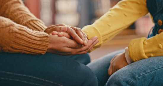 Woman consoling another woman and holding her hand.